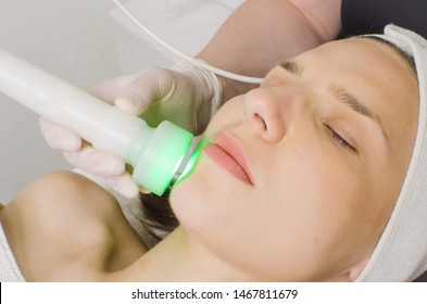 Beautician Doing Green Led Light Therapy To Female Customer In Beauty Salon, Facial Photo Therapy For Skin Pore Cleansing. Anti-aging Treatments And Photo Rejuvenation Procedure