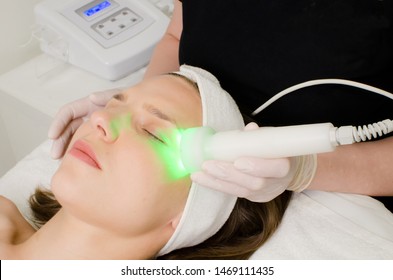 Beautician Doing Green Led Light Therapy To Female Customer In Beauty Salon, Facial Photo Therapy For Skin Pore Cleansing. Anti-aging Treatments And Photo Rejuvenation Procedure