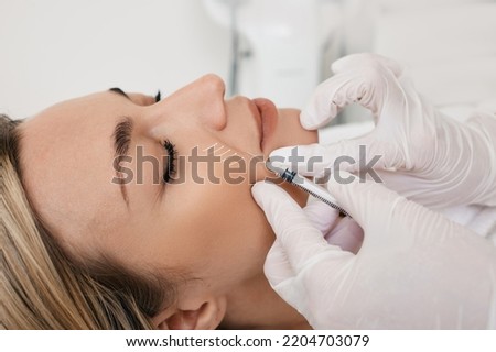Beautician doing injection into nasolabial folds to female patient. Correction of wrinkles on woman face using dermal fillers Foto stock © 
