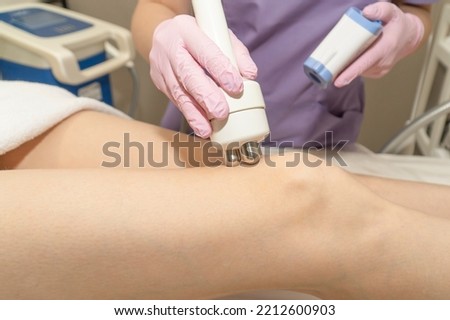 Beautician doing radio frequency leg lift for cellulite treatment, woman getting radio frequency skin tightening over knee in beauty salon, beautician working with radio frequency machine