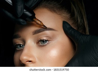 Beautician hand doing brow permanent makeup on an attractive female face
