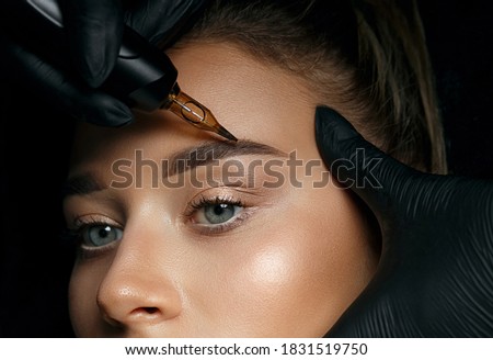 Beautician hand doing brow permanent makeup on an attractive female face
