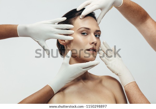 Beautician hands in gloves checking female face\
skin before aesthetic medical therapy. Woman going under cosmetic\
treatment on her facial\
skin.