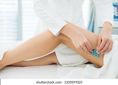 Beautician hands operating with eElectric device, sticking electrodes to female hips. Myostimulation session performed on the slim female legs with healthy skin