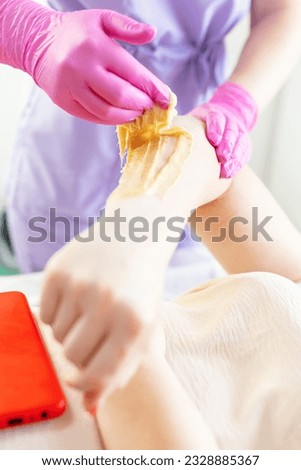 A beautician makes a sugar paste depilation of a woman's hand in a beauty salon. Female cosmetology. Removing unnecessary hair on the hand.  Sugar depilation. Depilatory sugar paste