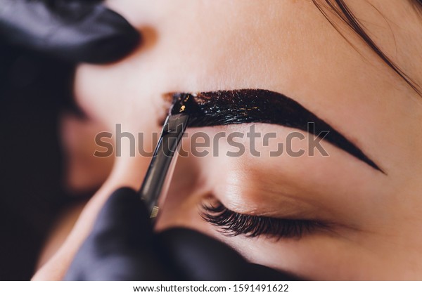 beautician- makeup artist
applies paint henna on previously plucked, design, trimmed eyebrows
in a beauty salon in the session correction. Professional care for
face.