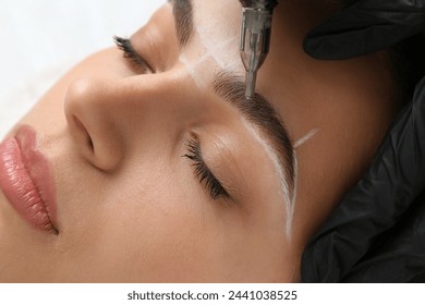 Beautician making permanent eyebrow makeup to young woman on white background, closeup - Powered by Shutterstock