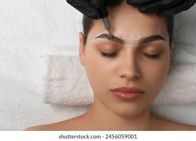 Beautician making permanent eyebrow makeup to young woman, top view. Space for text - Powered by Shutterstock