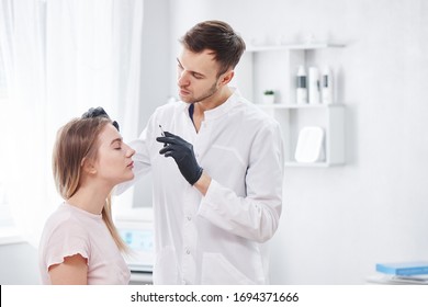 Beautician man gives beauty injections to young woman patient, handsome dermatologist puts disport in forehead wrinkles, face botox filler in the cosmetology salon - Shutterstock ID 1694371666