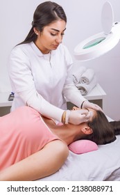 Beautician Performing Eyebrow Grooming, Young Woman Lying On Stretcher Receiving Beauty Treatment. High Quality Photo