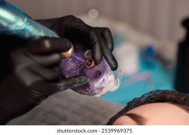 Beautician preparing to apply permanent makeup, picking up red pigment with a tattoo machine