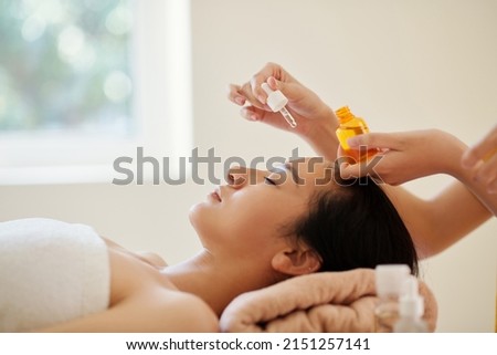 Beautician putting few drops of moisturizing oil on face of young woman