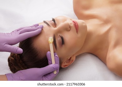 Beautician is removing hair from beautiful female face with hot wax. Woman has a beauty treament procedure. Depilation, epilation, skin and health care concepts. - Shutterstock ID 2117963306