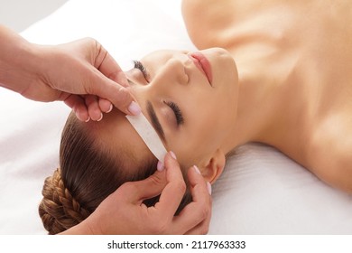 Beautician is removing hair from beautiful female face with hot wax. Woman has a beauty treament procedure. Depilation, epilation, skin and health care concepts.