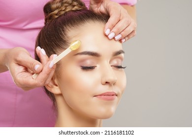 Beautician is removing hair from young female face with hot wax. Woman has a beauty treament procedure. Depilation, epilation, skin and health care concepts.