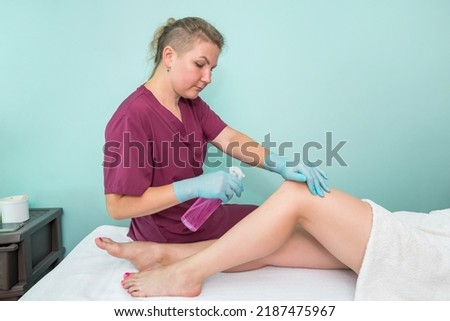 A beautician sprays a disinfectant on the feet of a young woman before the epilation procedure. Foot depilation