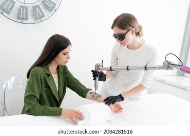 Beautician Using Laser Device To Remove An Unwanted Tattoo From Female Arm. Concept Of Erasing Tattoos As An Expensive Procedure In A Cosmetology Clinic