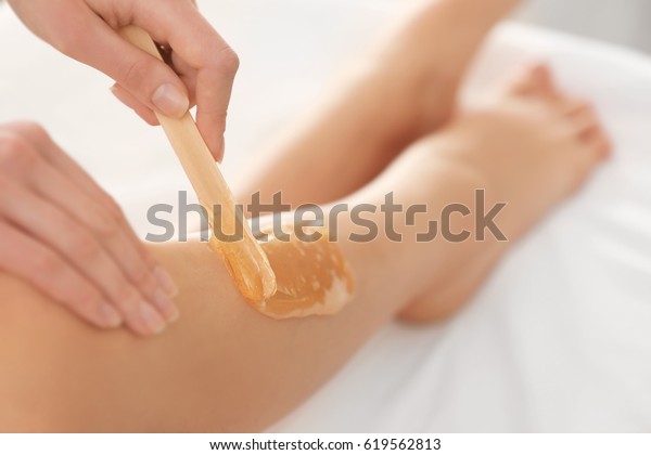 Beautician waxing female\
legs in spa center