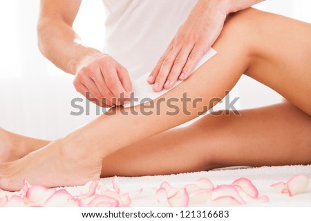Beautician waxing a woman's leg applying a strip of material over the hot wax to remove the hairs when pulled