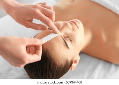 Beautician Waxing Young Woman's Eyebrows In Spa Center