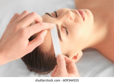 Beautician Waxing Young Woman's Eyebrows In Spa Center