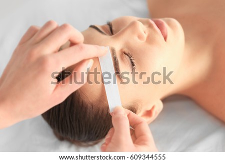 Beautician waxing young woman's eyebrows in spa center