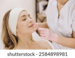 Beautician wearing pink gloves carefully applying lip mask to relaxed female client resting on treatment bed during skincare procedure