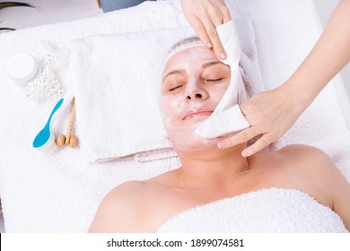 The beautician wipes the mask from the senior woman's face, close-up portrait. Beautician makes a facial skin care procedure. Spa and beauty