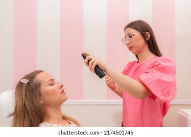 A beautician woman applying spray foundation to her client at the beauty salon