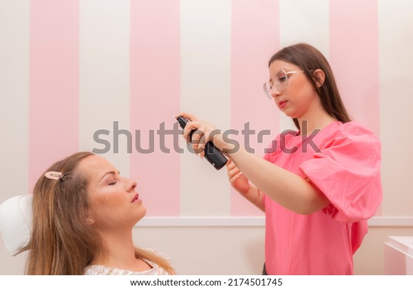 A beautician woman applying spray foundation\
to her client at the beauty\
salon