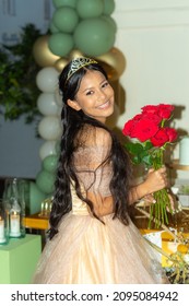 beautiful 15 year old girl celebrates her birthday with a tiara and an elegant dress and a bouquet of red roses

