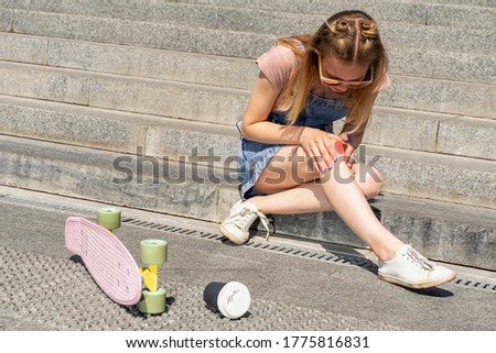 beautiful 16 years teenager girl with knee injury on the stone steps with a skateboard. dangerous sports in the city