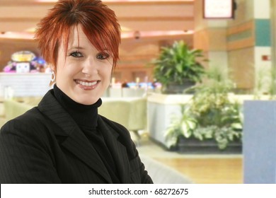 Beautiful 30 Year Old Business Woman In Black Suit With Smiling  Expression In Hotel Lobby.