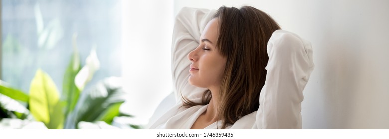 Beautiful 30s woman closed eyes put hands behind head relaxing on comfortable sofa in cozy warm light living room with houseplants, no stress concept, horizontal photo banner for website header design - Powered by Shutterstock