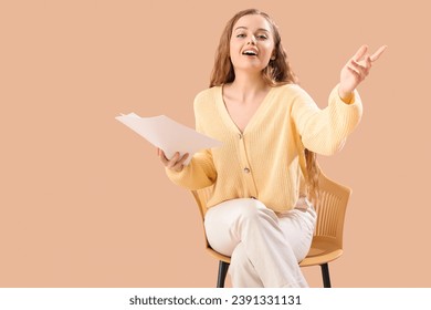 Beautiful actress with film script in chair on beige background