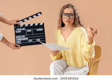 Beautiful actress with film script in chair and movie clapper on beige background - Powered by Shutterstock