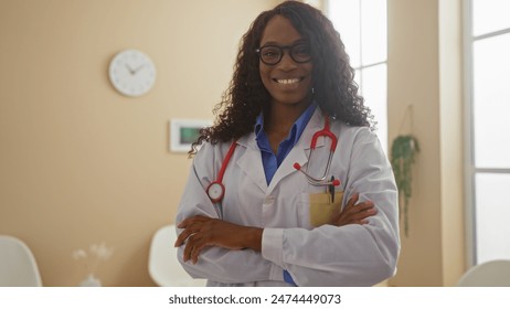 A beautiful adult african american woman with curly hair and glasses, dressed as a doctor with crossed arms, stands confidently in a clinic waiting room. - Powered by Shutterstock