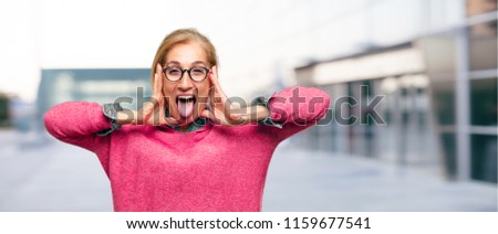 Beautiful adult blonde woman joking, sticking tongue out with a funny, silly and playful expression, looking like a fool.