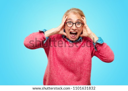 Beautiful adult blonde woman shouting with a crazy, amazed look of surprise, holding head with both hands.