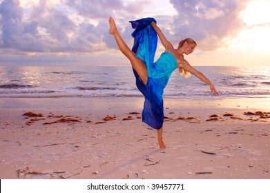 A Beautiful Adult Female Ballerina Is Dancing On The Beach With Her Leg Kicked Up High And Balanced On One Foot As The Sun Begins To Set