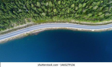 Beautiful Aerial View Of Road Between Green Summer Forest And Blue Lake In Lapland.