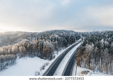 Beautiful aerial view of snow covered fields with a two-lane road among trees. Rime ice and hoar frost covering trees. Scenic winter landscape near Vilnius, Lithuania.