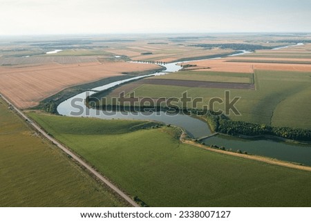 Beautiful aerialview with a country road next to a lake and big agriculture fields. Concept video for summer agriculture and transportation industry.