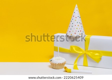 Beautiful and aesthetic birthday set with space for your design and text. Cupcake with white cream and one candle, gift and horn on white table. Happy Birthday card design concept.