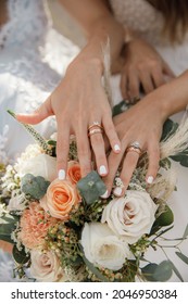 beautiful aesthetic same sex wedding two brides lesbian hold hands with wedding rings and bouquet with orange and white roses close up on a sunny day 