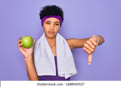 Beautiful African American Afro Sporty Woman Doing Exercise Wearing Towel Eating Green Apple With Angry Face, Negative Sign Showing Dislike With Thumbs Down, Rejection Concept