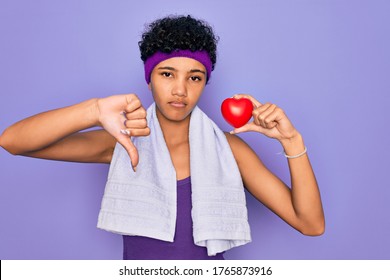 Beautiful African American Afro Sporty Woman Doing Exercise Wearing Towel Holding Heart With Angry Face, Negative Sign Showing Dislike With Thumbs Down, Rejection Concept