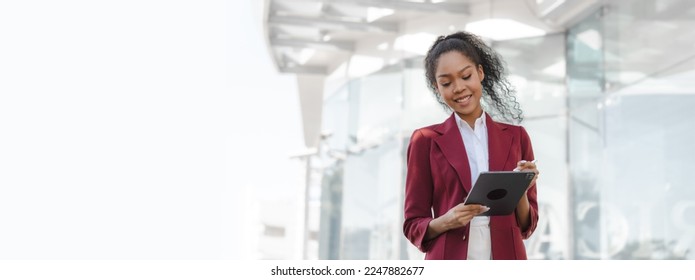 Beautiful african american business woman in red formal suit leader entrepreneur, professional manager holding digital tablet, going to work, walking urban outdoor, standing on city street - Powered by Shutterstock