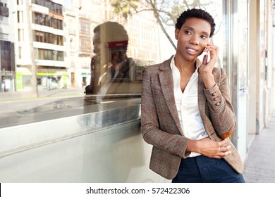 Beautiful African American Business Woman With Office Building Glass With City Reflections, Smiling Outdoors. Professional Black Woman In Smart Phone Conversation Call, Lifestyle Technology.