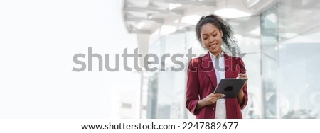 Beautiful african american business woman in red formal suit leader entrepreneur, professional manager holding digital tablet, going to work, walking urban outdoor, standing on city street